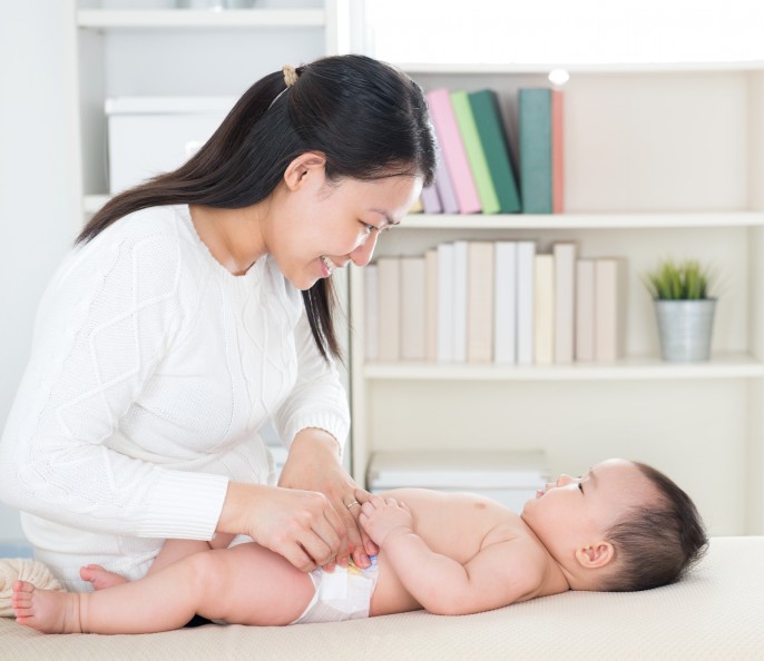 Asian mother changing diaper to baby girl at home.